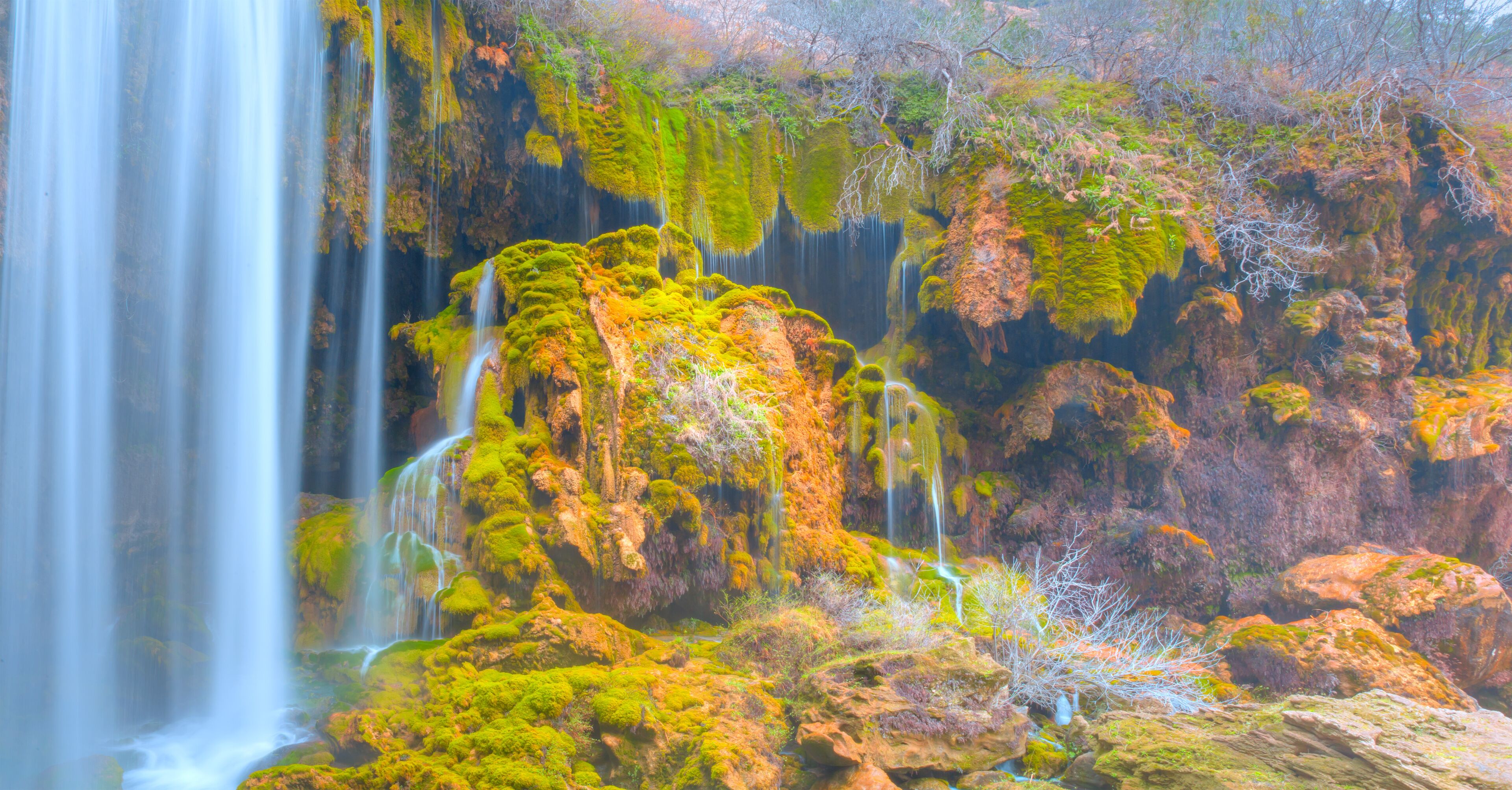 A waterfall cascading over moss-covered rocks in a forested area.