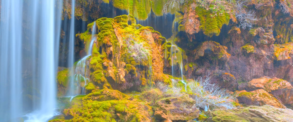A waterfall cascading over moss-covered rocks in a forested area.