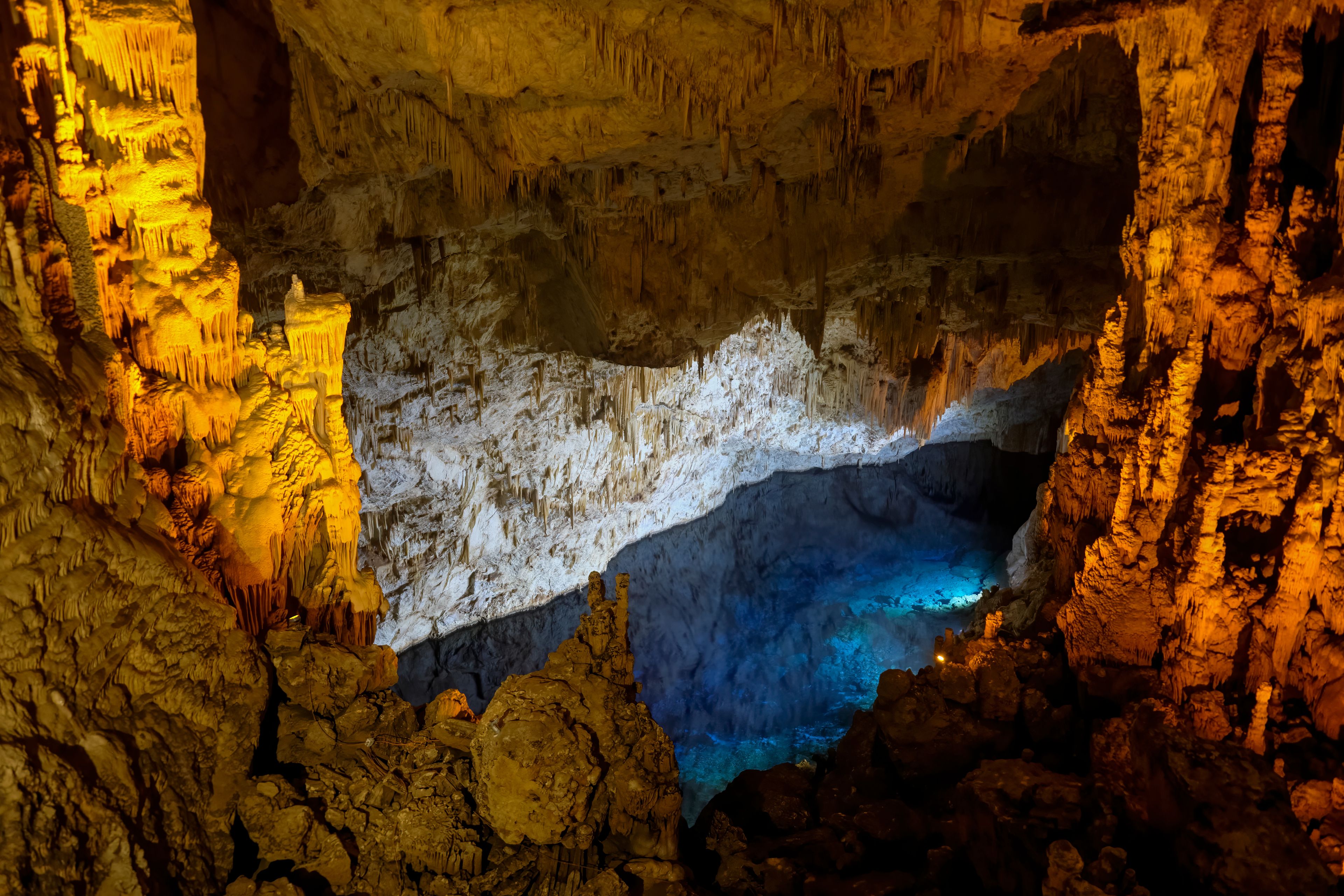 A cave with stalactites and stalagmites, illuminated by artificial lighting.