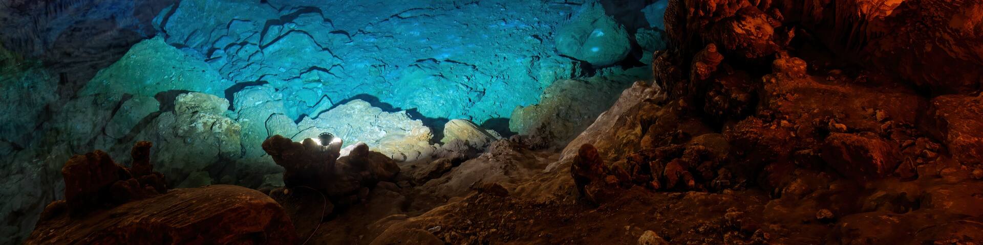 A cave with stalactites and stalagmites, illuminated by artificial lighting.