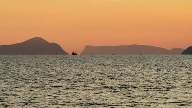 A calm sea at sunset with distant mountains silhouetted against the sky.