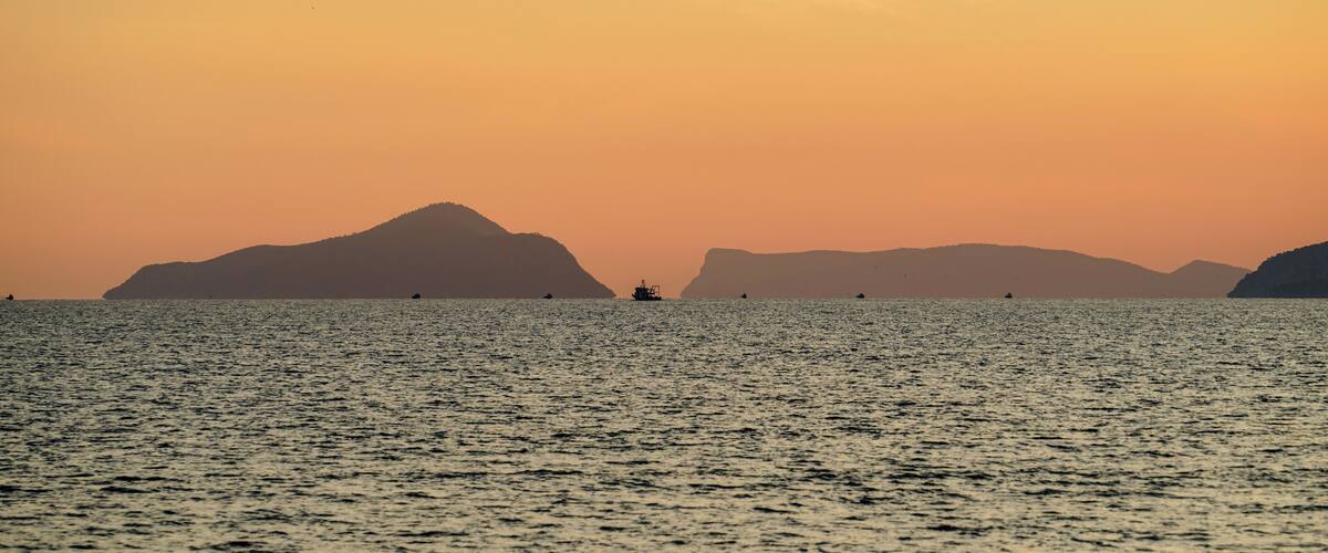 A calm sea at sunset with distant mountains silhouetted against the sky.
