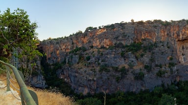 A rugged mountain with a cave entrance, surrounded by greenery and a clear sky.