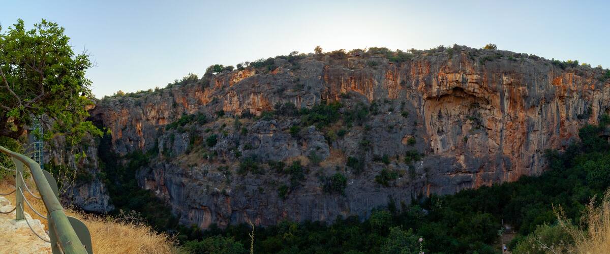 A rugged mountain with a cave entrance, surrounded by greenery and a clear sky.