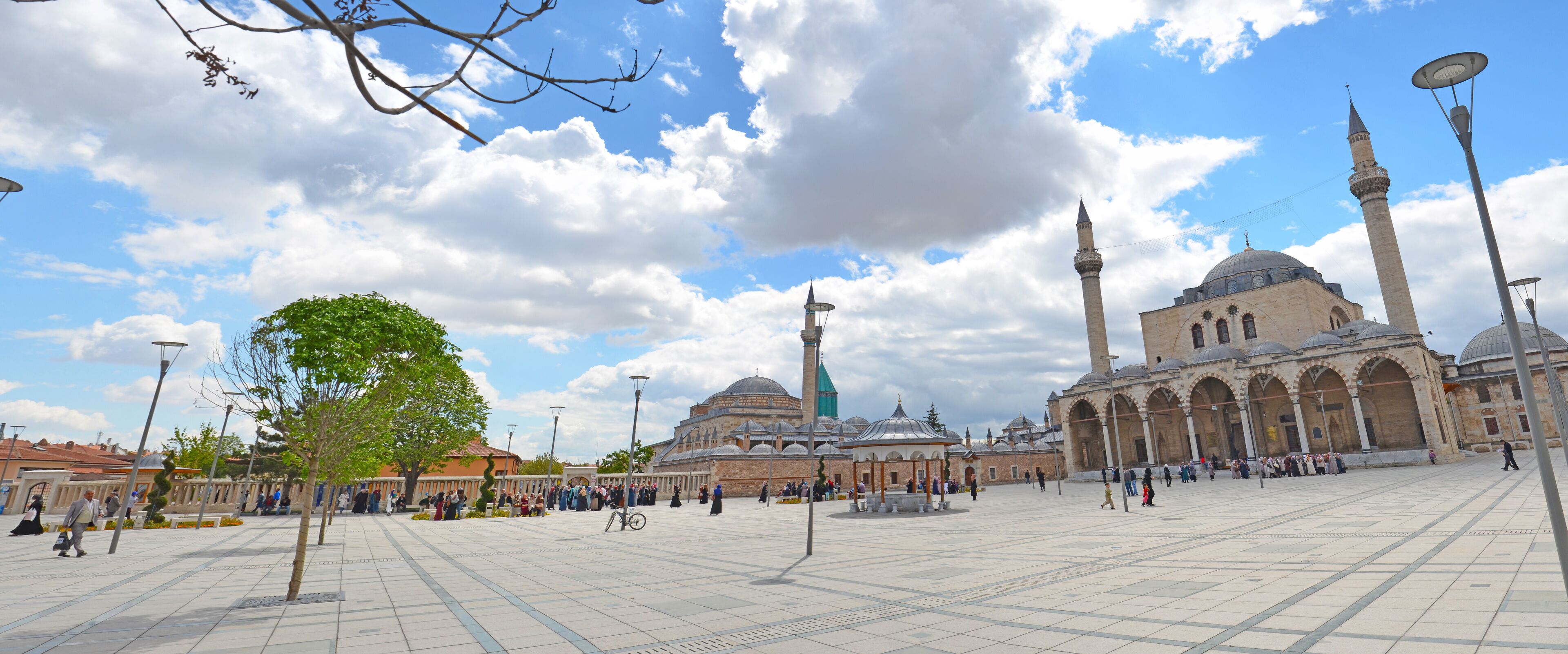 A mosque with two minarets and a large dome, surrounded by a spacious courtyard with people walking around.