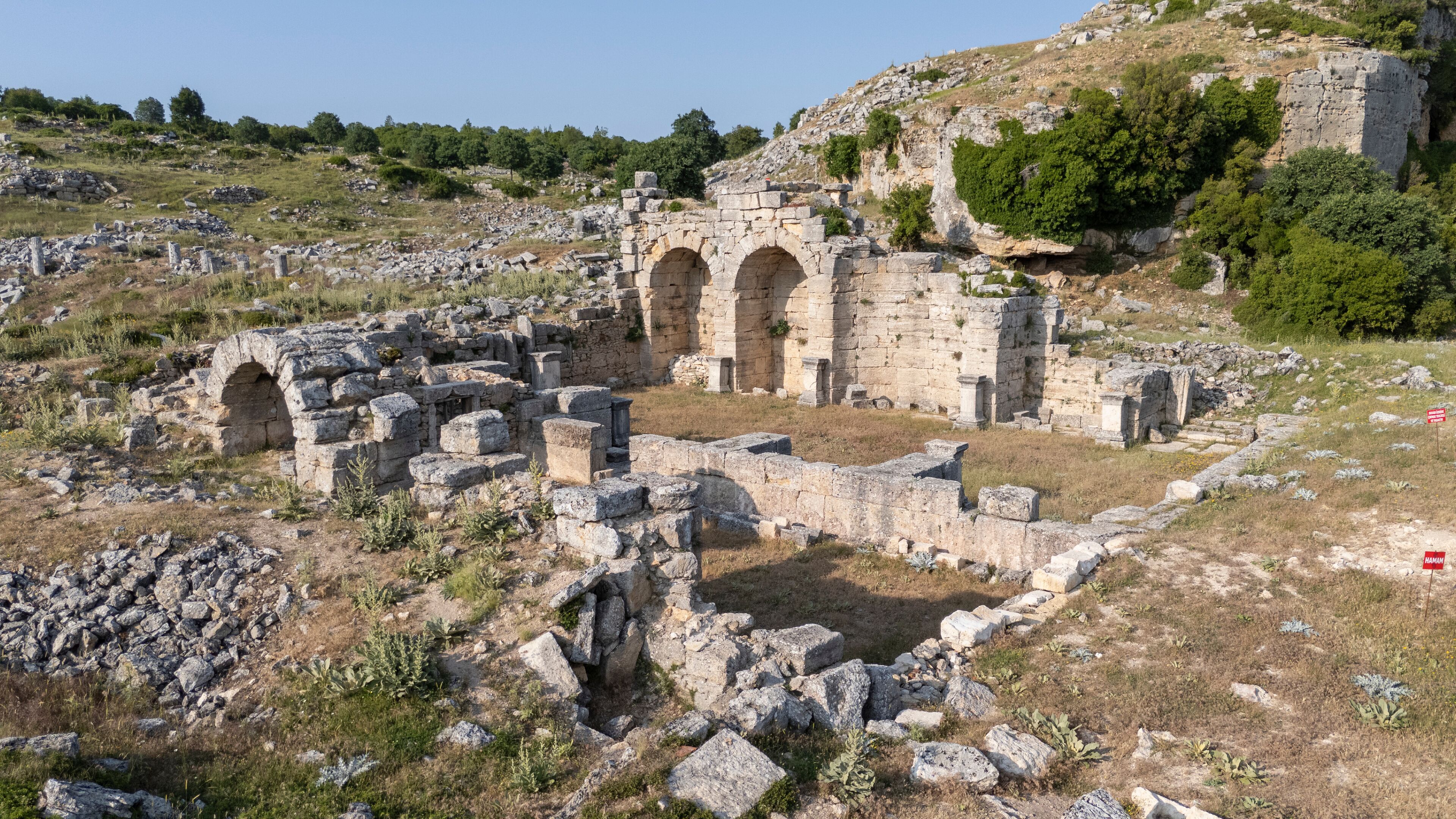 Ancient ruins with stone arches and scattered stones on a hillside.