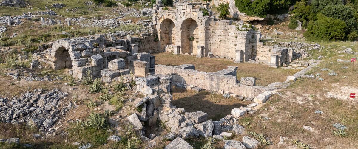 Ancient ruins with stone arches and scattered stones on a hillside.