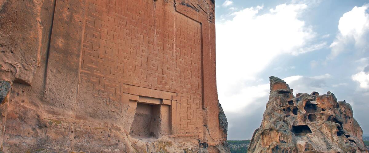 A large ancient brick structure with a carved doorway and a rock formation with multiple openings.