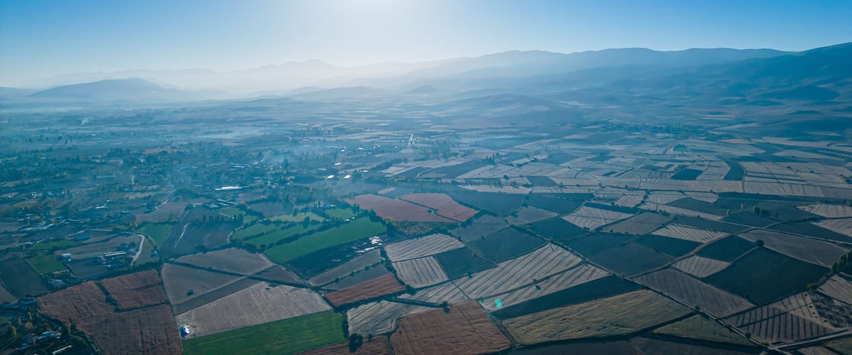 An aerial view of a rural landscape with fields, roads, and distant mountains under a clear sky.