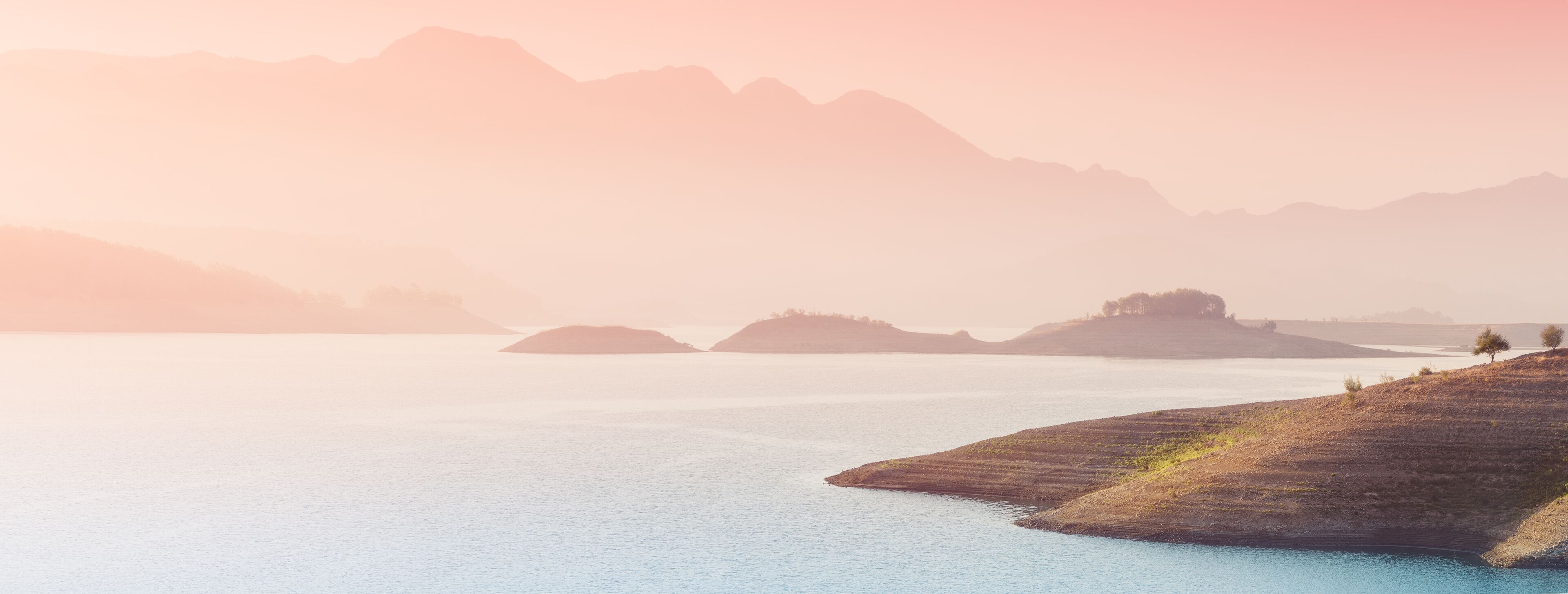 A calm lake with distant mountains and small islands.