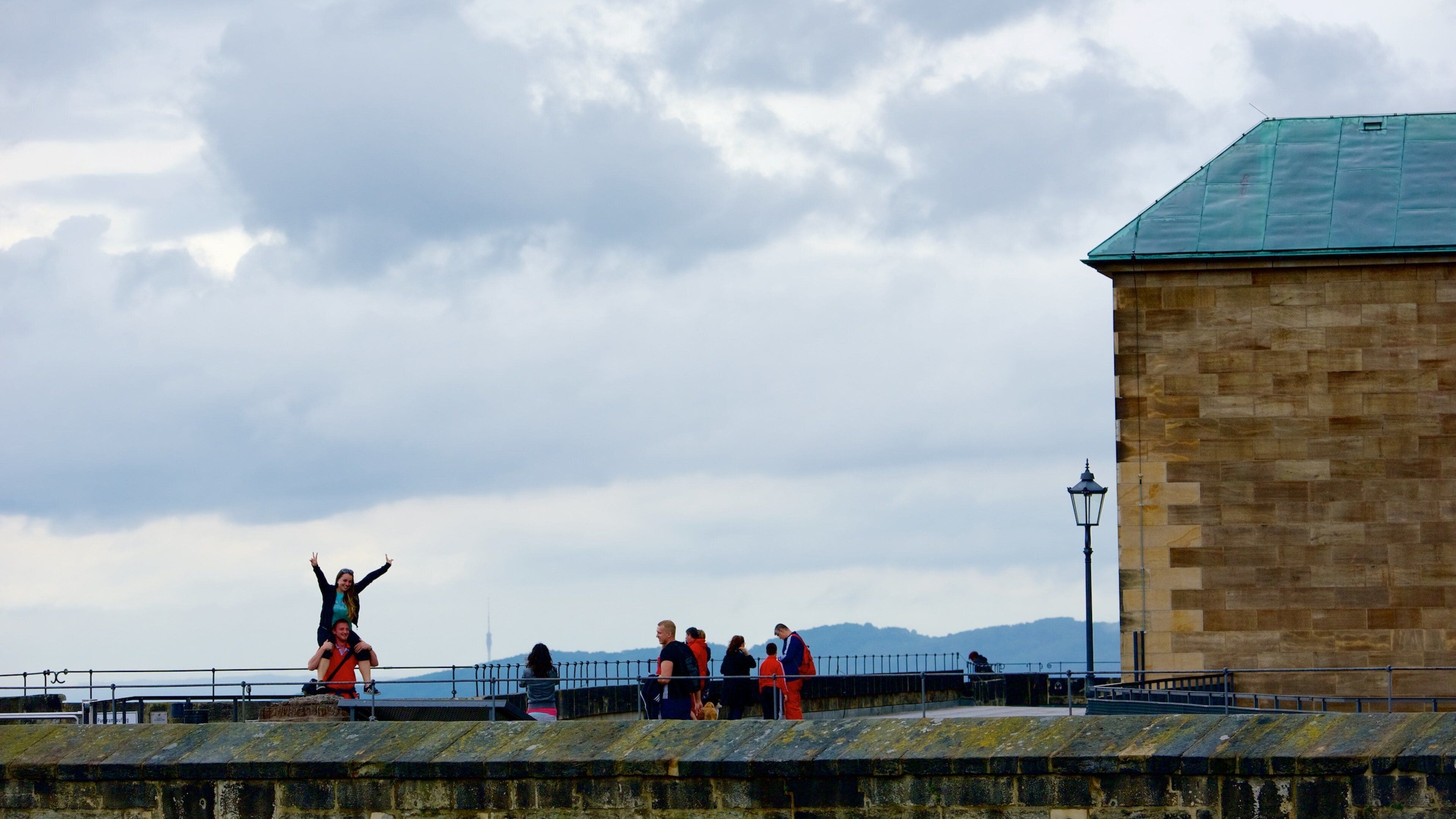 A stone building with a green roof, a metal railing, and a cloudy sky.