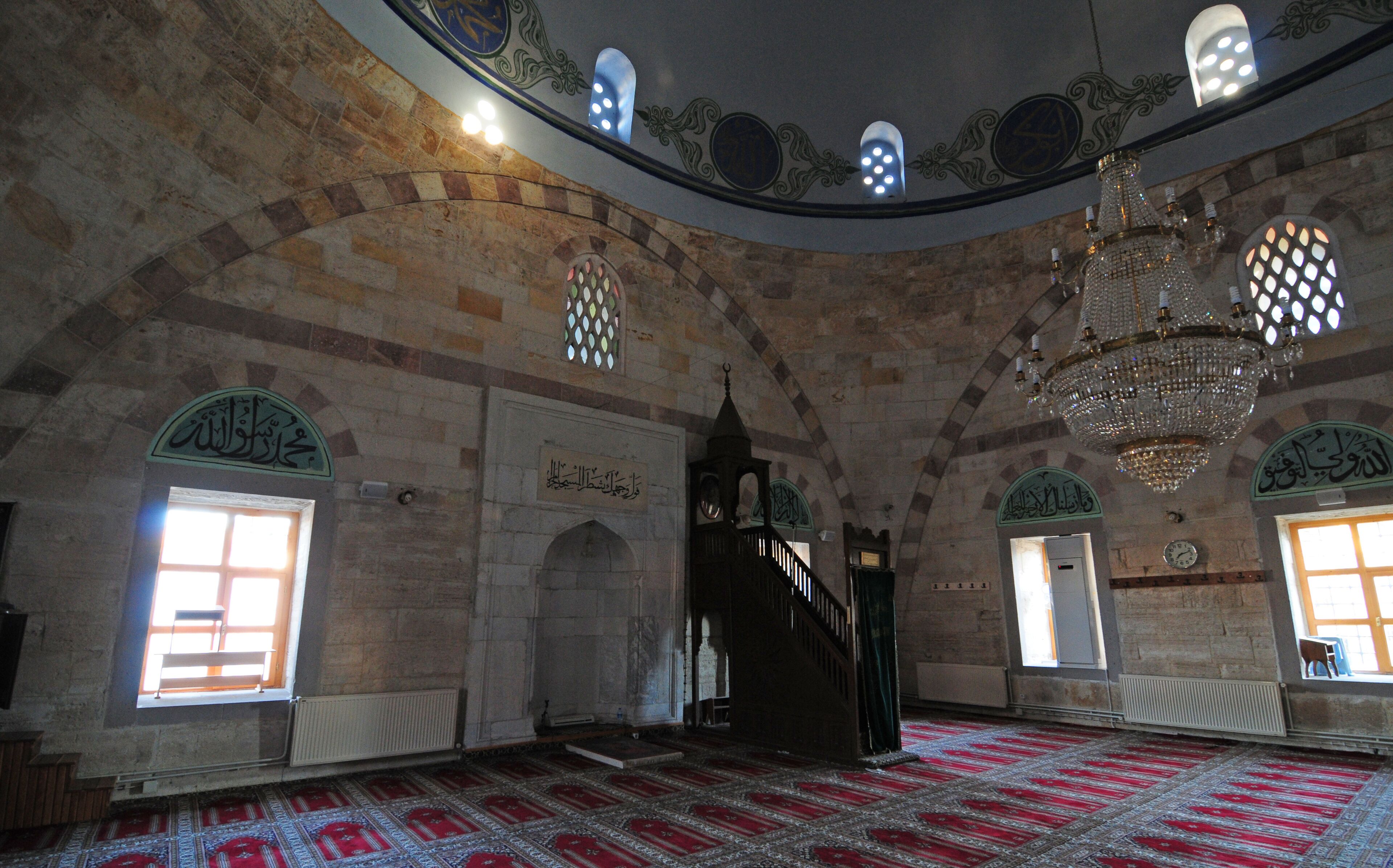 An interior with arched ceilings, a chandelier, and patterned carpets.