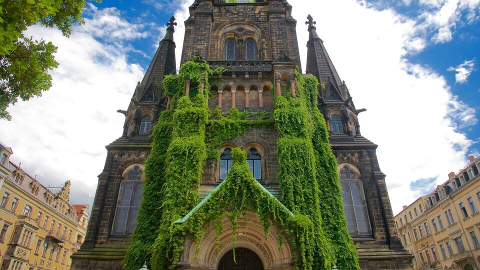 A historic building with intricate architecture, featuring a prominent tower and arched windows, partially covered in green ivy.