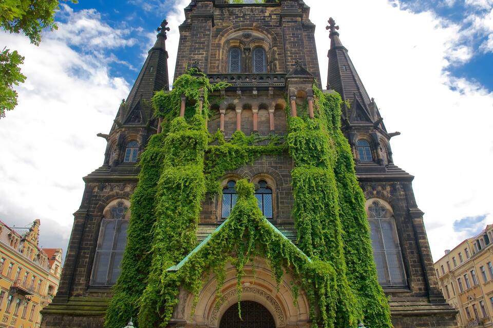 A historic building with intricate architecture, featuring a prominent tower and arched windows, partially covered in green ivy.