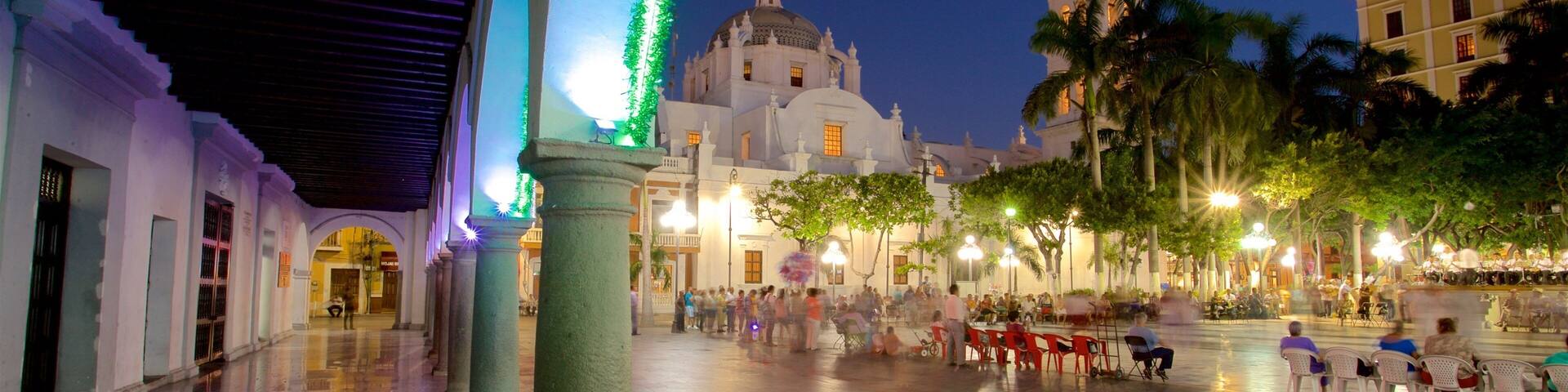 A historic plaza with colonial architecture, palm trees, and a large building with a dome and bell tower.