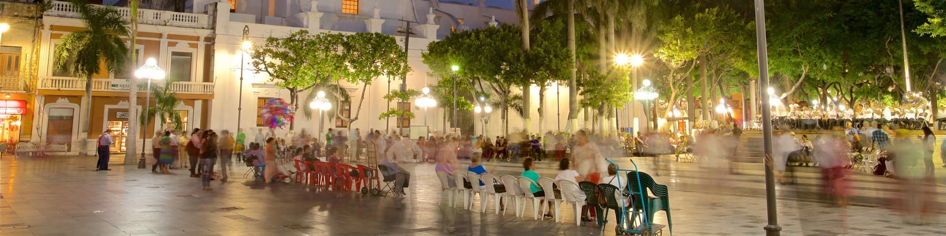 A plaza with a large white building featuring domes and a bell tower, surrounded by palm trees and street lamps.