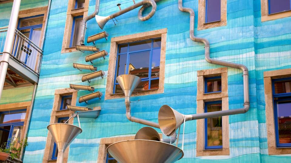 A building with blue and beige walls, multiple windows, and several metal funnels and pipes attached to the exterior.
