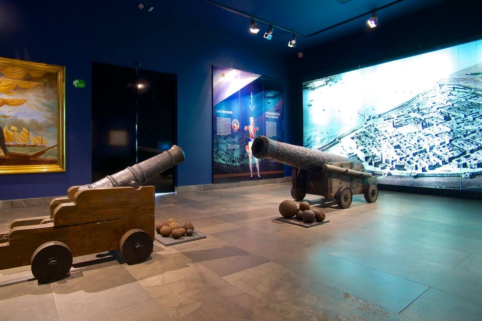 A museum exhibit with cannons and a large painting on the wall.