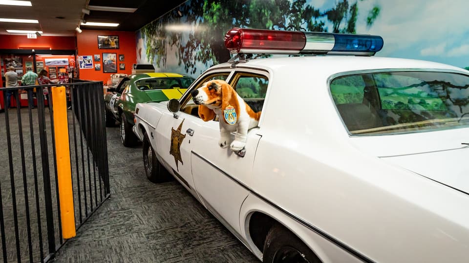 Ein weißes Polizeiauto mit Hundeaufkleber an der Seite, geparkt in einem Gebäude mit einer Baum-Muralwand.