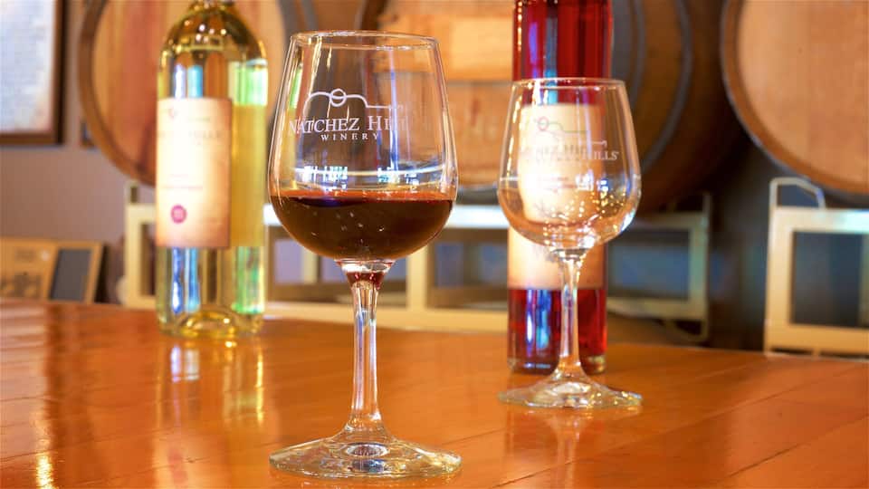 Two wine glasses on a wooden table with a wine bottle and barrels in the background.