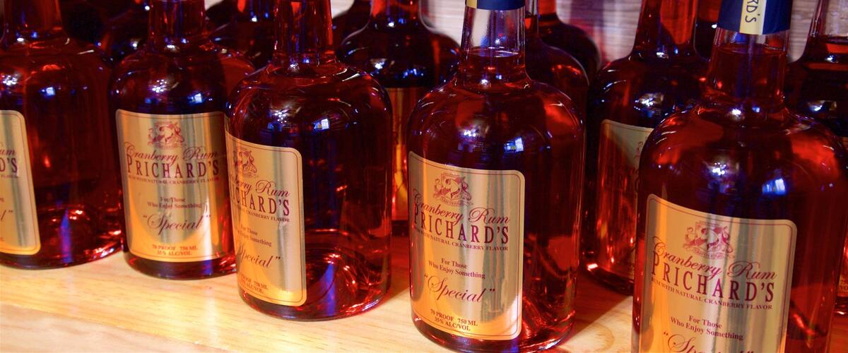 Multiple bottles of Prichard's Cranberry Rum on a wooden shelf.