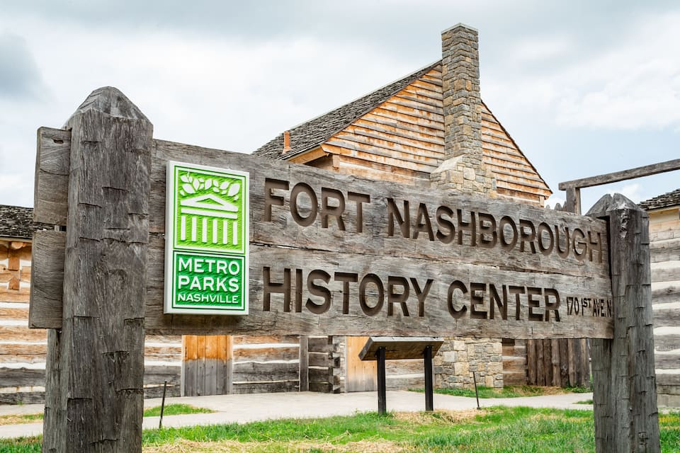 Un senyal de fusta del Fort Nashborough History Center, amb un edifici de pedra al fons.