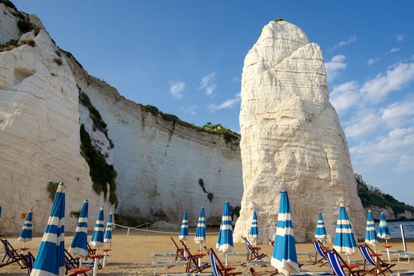 Une plage bordée de falaises blanches et ombragée par des parasols rayés de bleu.