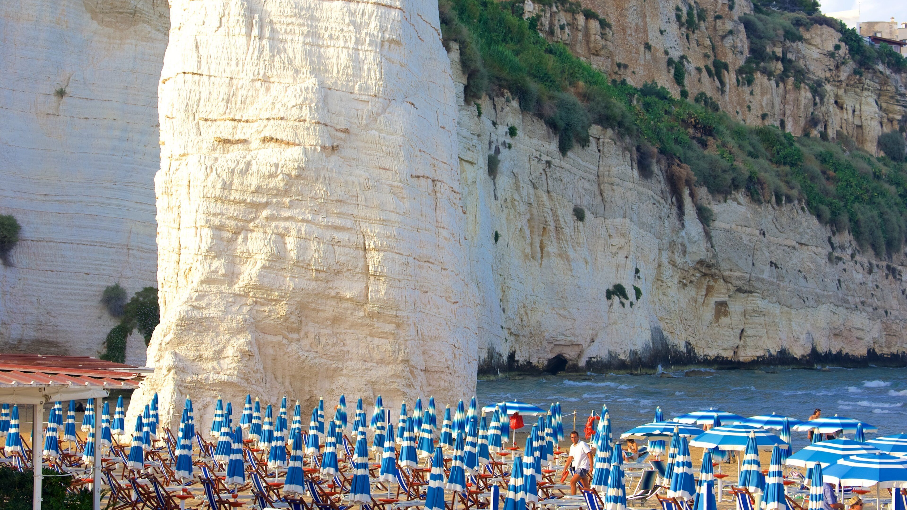 A beach with white cliffs and blue umbrellas.