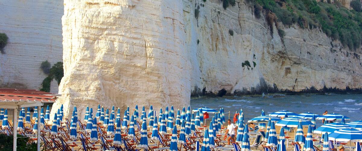 A beach with white cliffs and blue umbrellas.