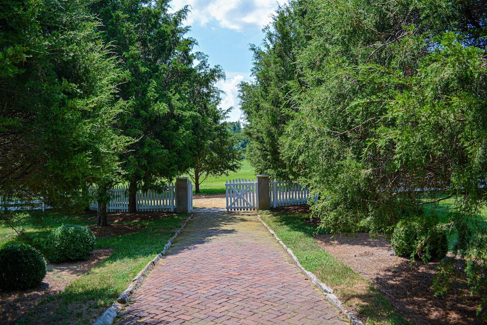A brick pathway leading to a gated entrance surrounded by lush green trees.