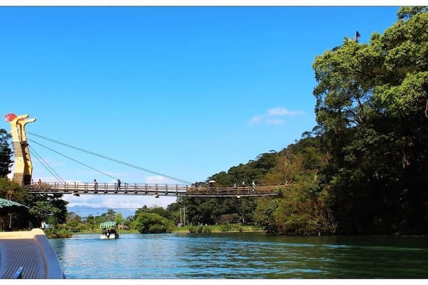 Un pont suspendu enjambant une rivière, entouré d’une végétation luxuriante et d’arbres.