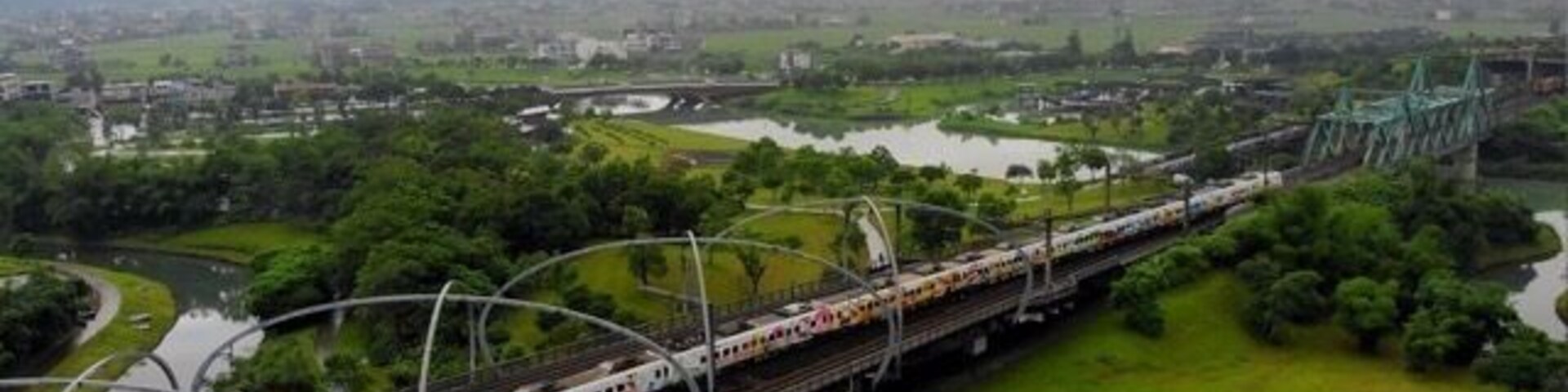 Un tren sobre vías elevadas con follaje y un río al fondo.