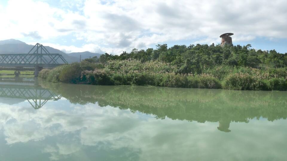 A calm lake reflecting a bridge and a hill with a structure on top.