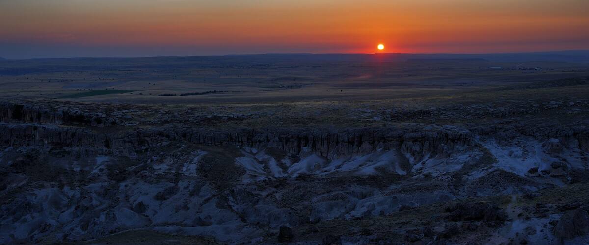 A sunset over a vast, flat landscape with a snow-covered foreground and a clear sky.