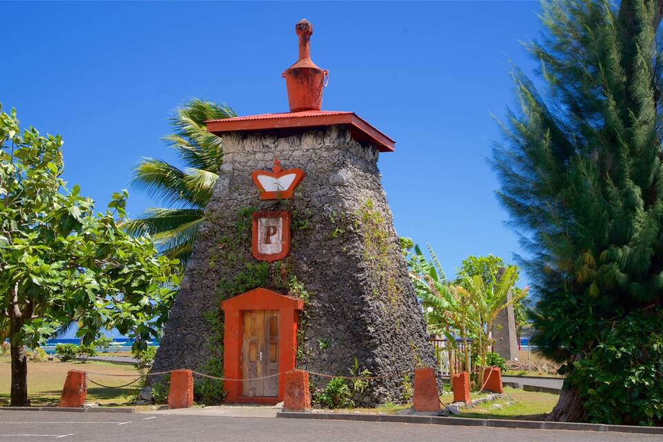 Une petite tour de pierre, surmontée d’un toit rouge et dotée d’une porte en bois, entourée de palmiers et s’élevant vers un ciel d’un bleu limpide.