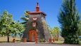 A small stone tower with a red roof and a wooden door, surrounded by palm trees and a clear blue sky.