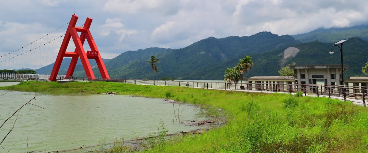 A red bridge over a river with mountains in the background.