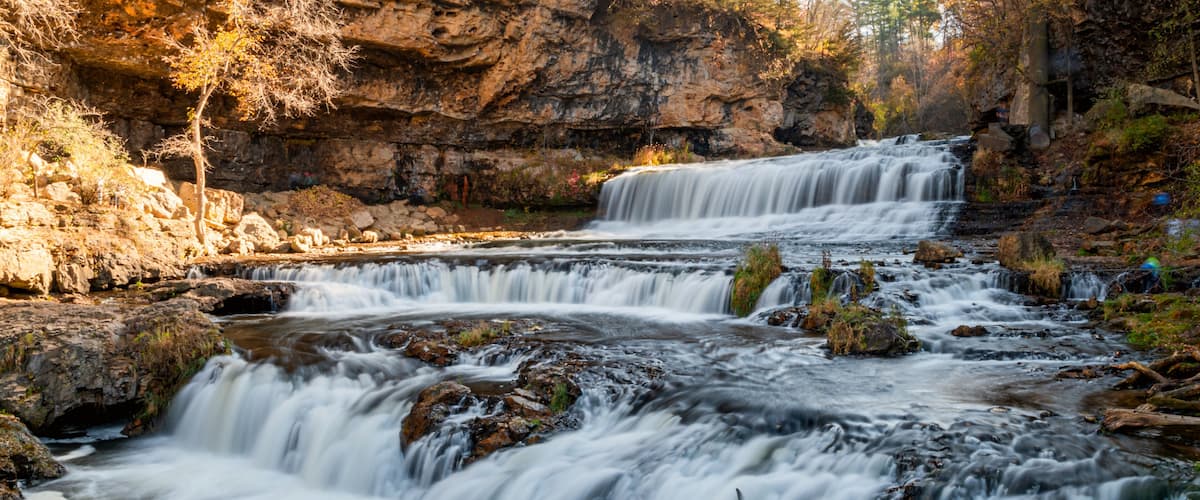 A multi-tiered waterfall surrounded by rocky terrain and autumn foliage.