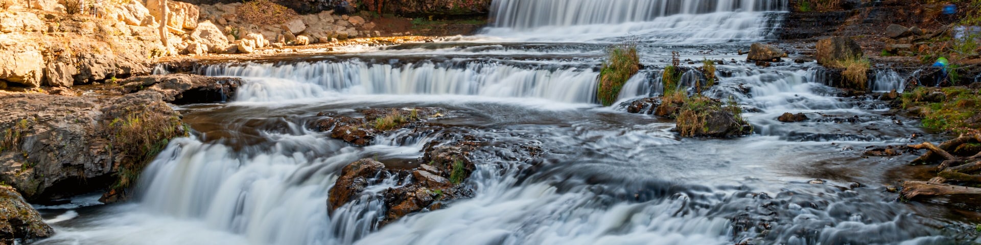 A multi-tiered waterfall surrounded by rocky terrain and autumn foliage.