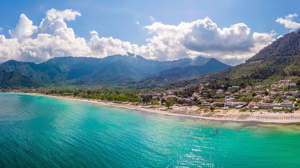 Eine Küstenstadt mit türkisblauem Wasser, einem Sandstrand und Bergen im Hintergrund.