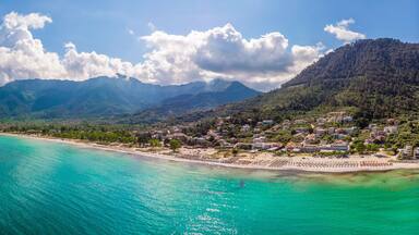 A coastal town with turquoise waters, a sandy beach, and mountains in the background.