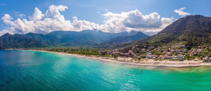 Un pueblo costero con aguas turquesas, una playa de arena y montañas al fondo.