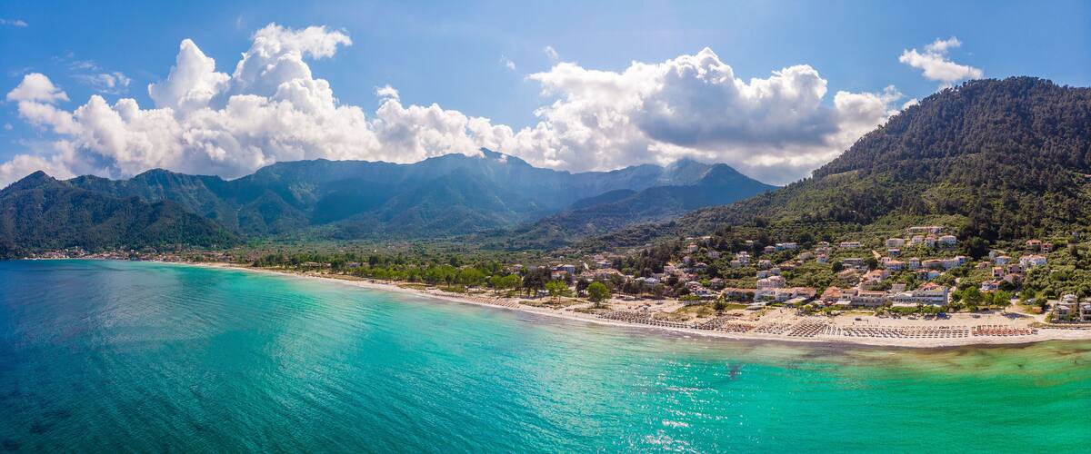 A coastal town with turquoise waters, a sandy beach, and mountains in the background.