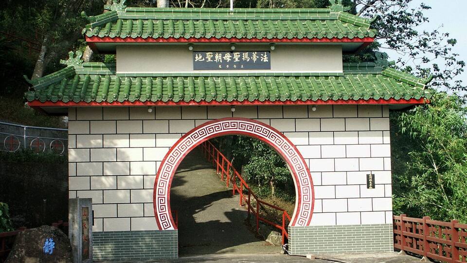 A traditional Chinese gate with a red arch and green roof, leading to a staircase.