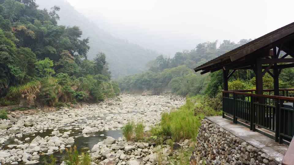 A rocky river with a wooden bridge and lush greenery.