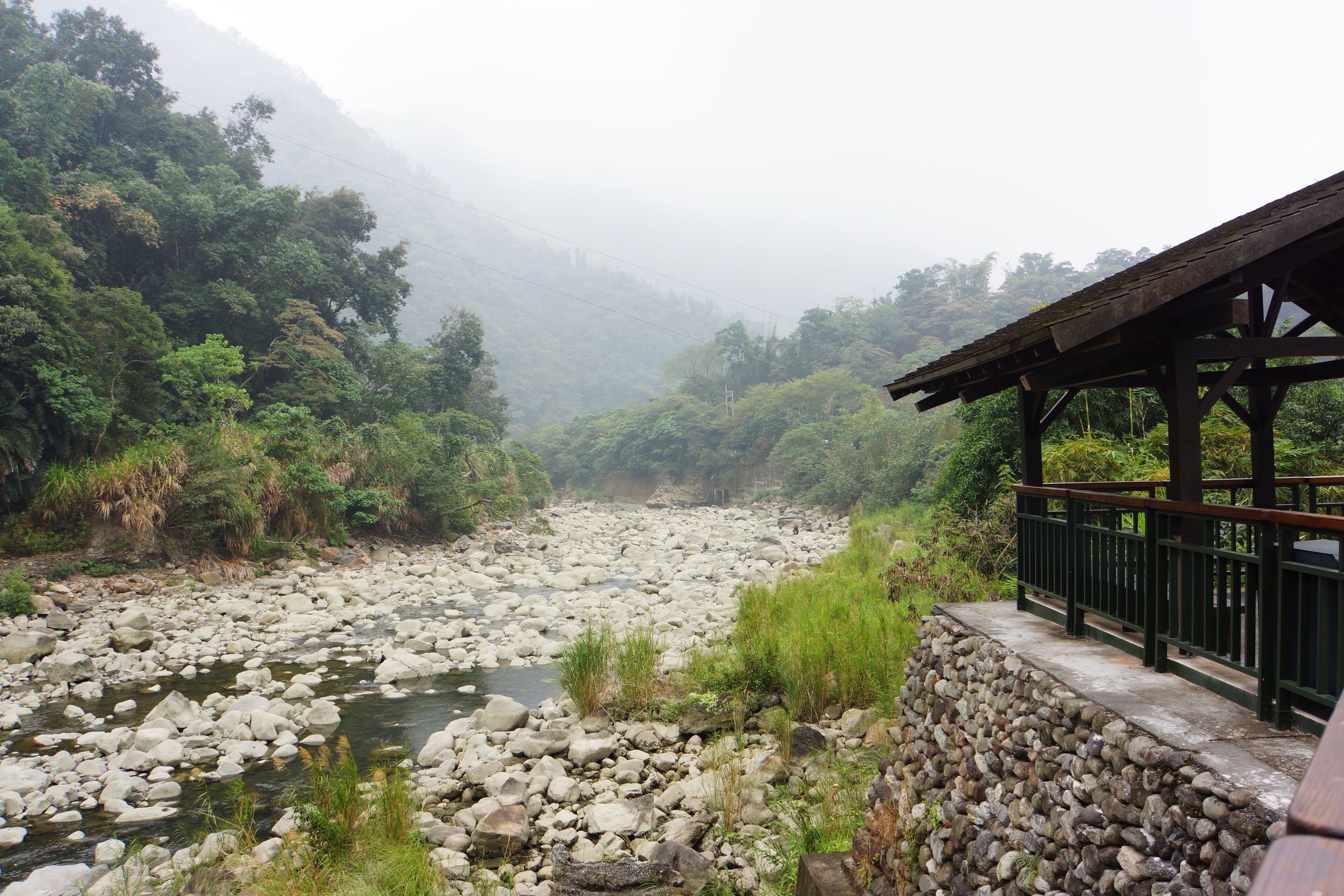 A rocky river with a wooden bridge and lush greenery.