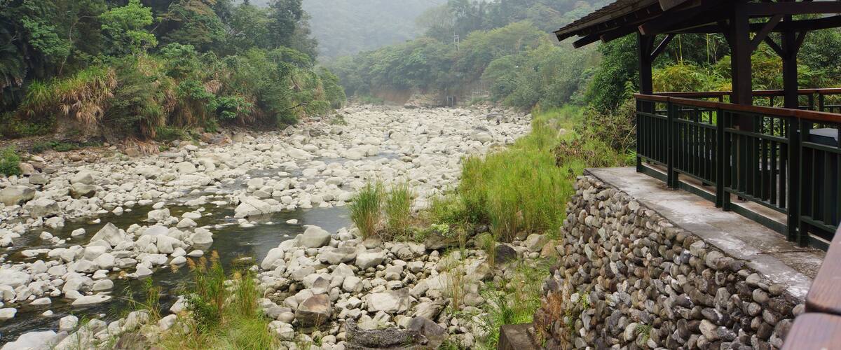 A rocky river with a wooden bridge and lush greenery.