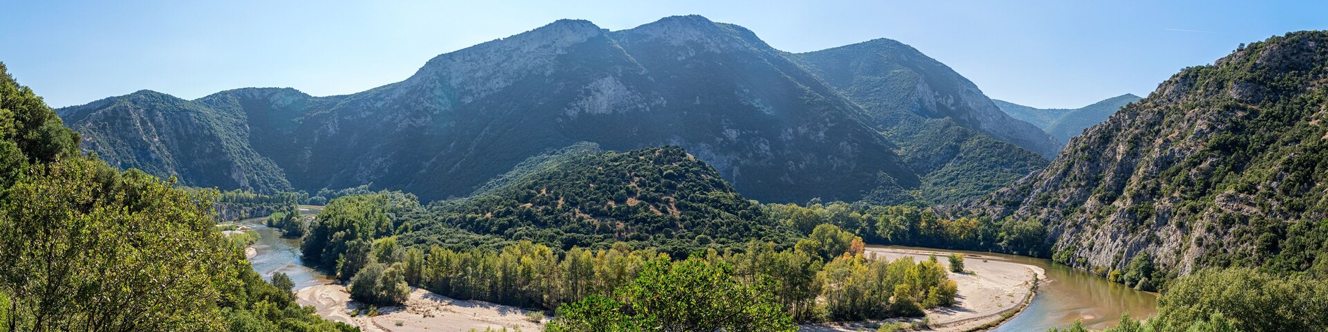 Un río serpentea a través de un paisaje montañoso con abundante follaje verde y terreno rocoso.