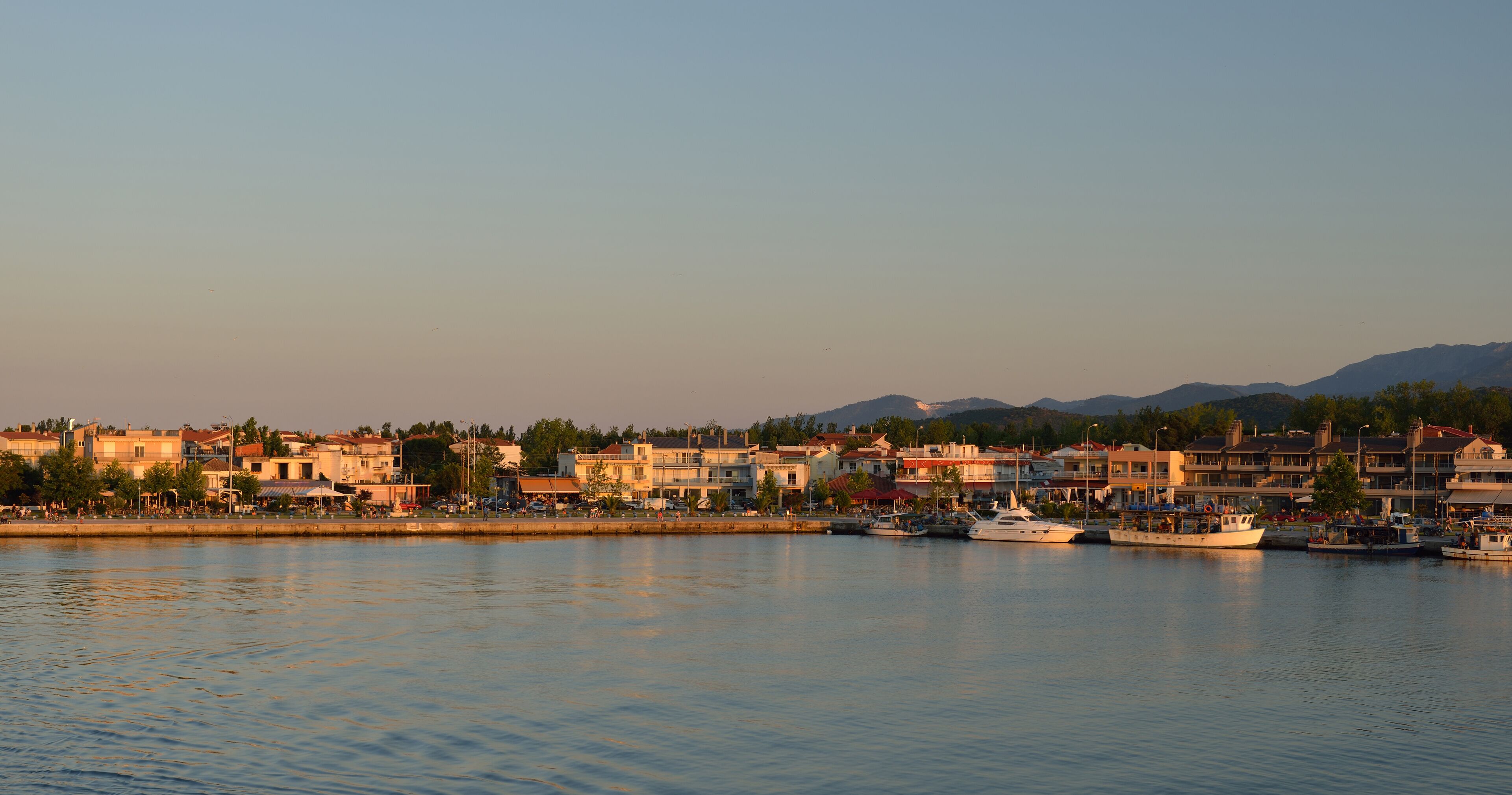 A coastal town with buildings, a marina, and mountains in the background.