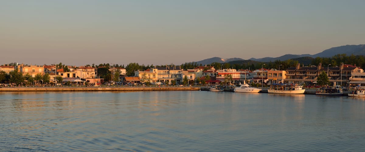 A coastal town with buildings, a marina, and mountains in the background.